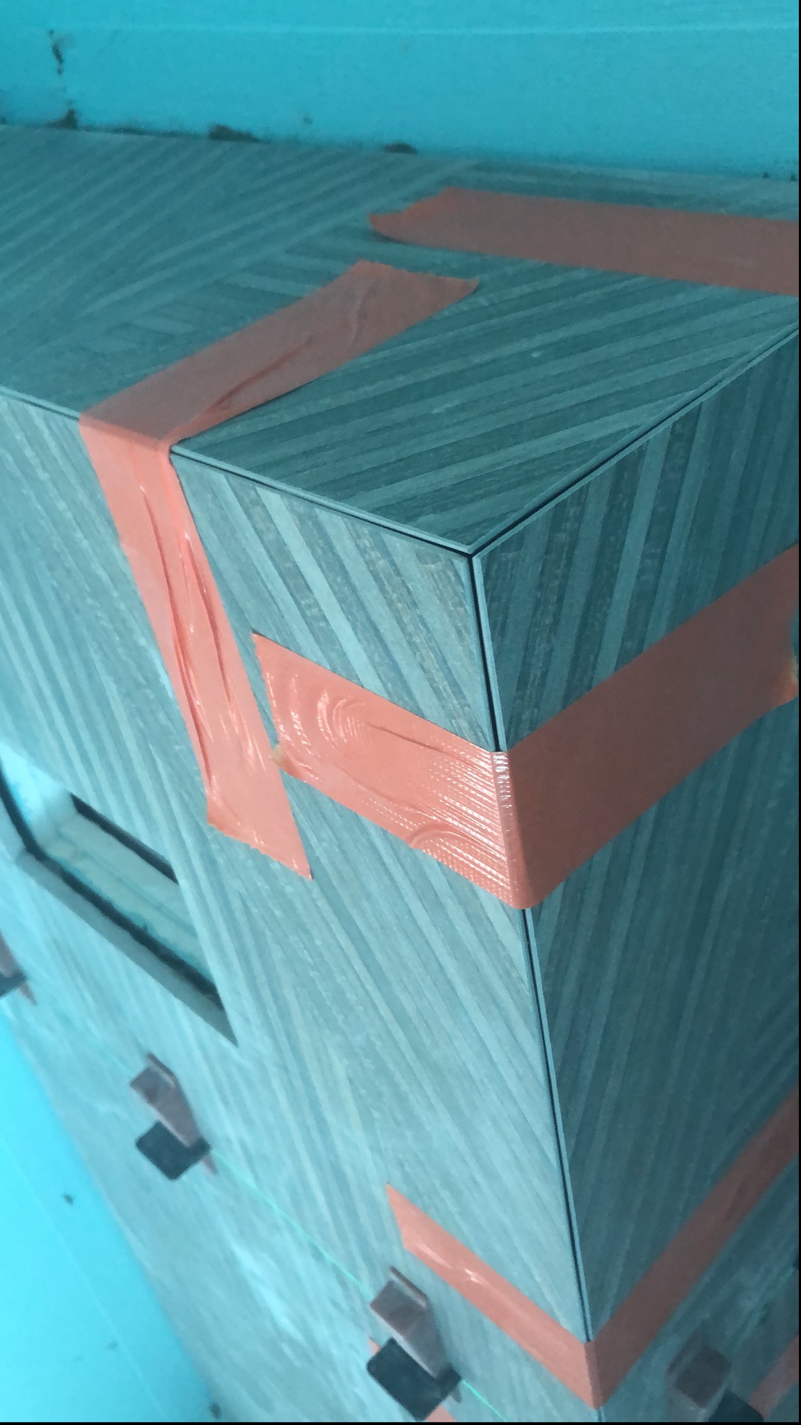 Fragment obudowy w łazience wyłożonej płytkami w odcieniach szarości, zabezpieczonej pomarańczową taśmą malarską i poziomowana przy użyciu klipsów dystansowych.