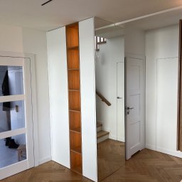 Visual trend meble na wymiar - Nowoczesna zabudowa przedpokoju z szafą z białymi frontami i otwartymi półkami z drewna, lustrzane drzwi odbijają schody, parkiet ułożony we wzór jodełki.