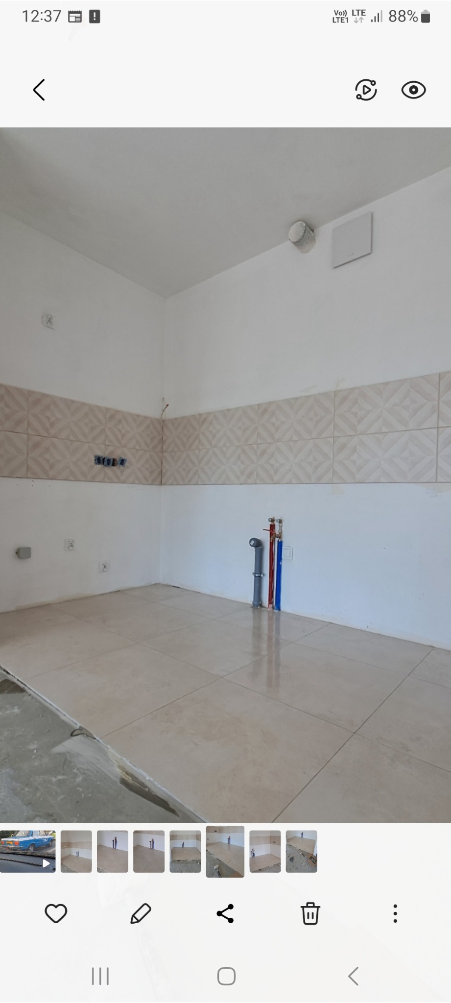 Świeżo wykafelkowana podłoga i ściany w łazience, z widocznymi przyłączami wodnymi i kanalizacyjnymi, oraz częściowo przygotowanym podłożem pod dalsze prace wykończeniowe.