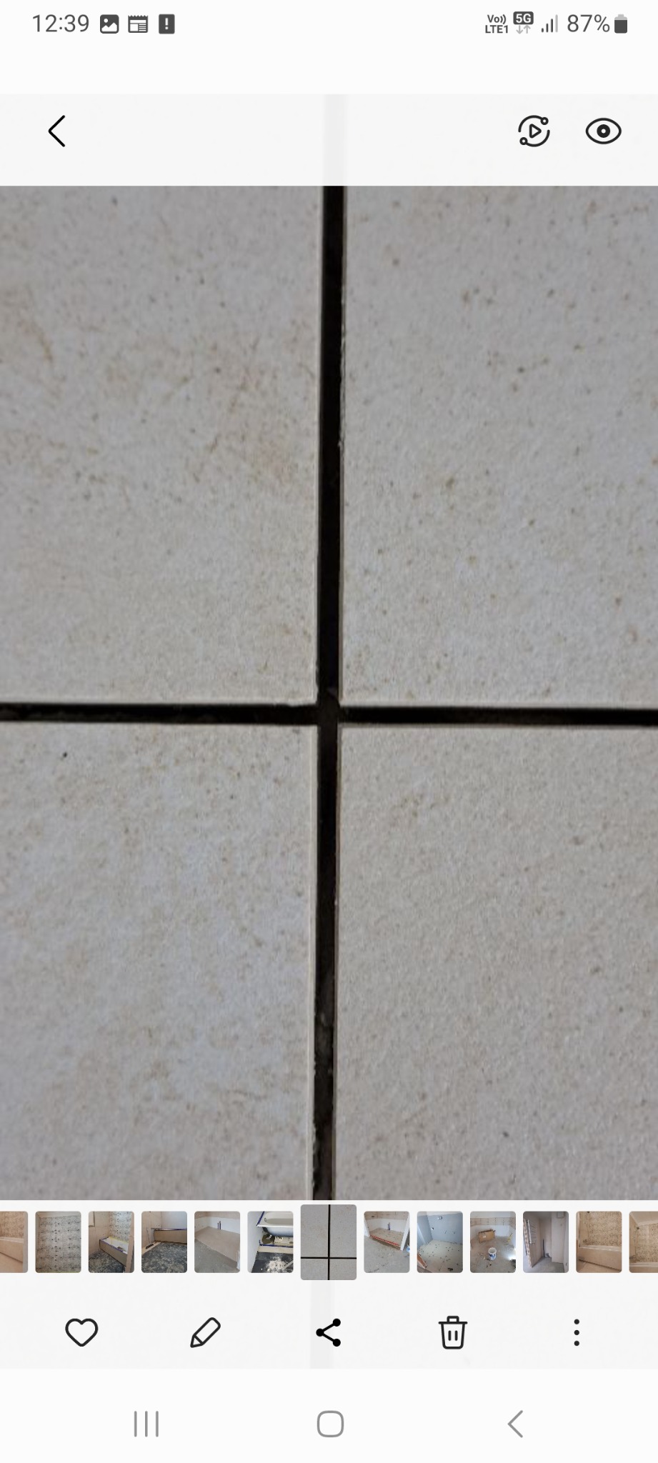 Zbliżenie na jasne, kwadratowe płytki z ciemnymi fugami tworzącymi krzyż, widoczne drobne zabrudzenia na powierzchni płytek.