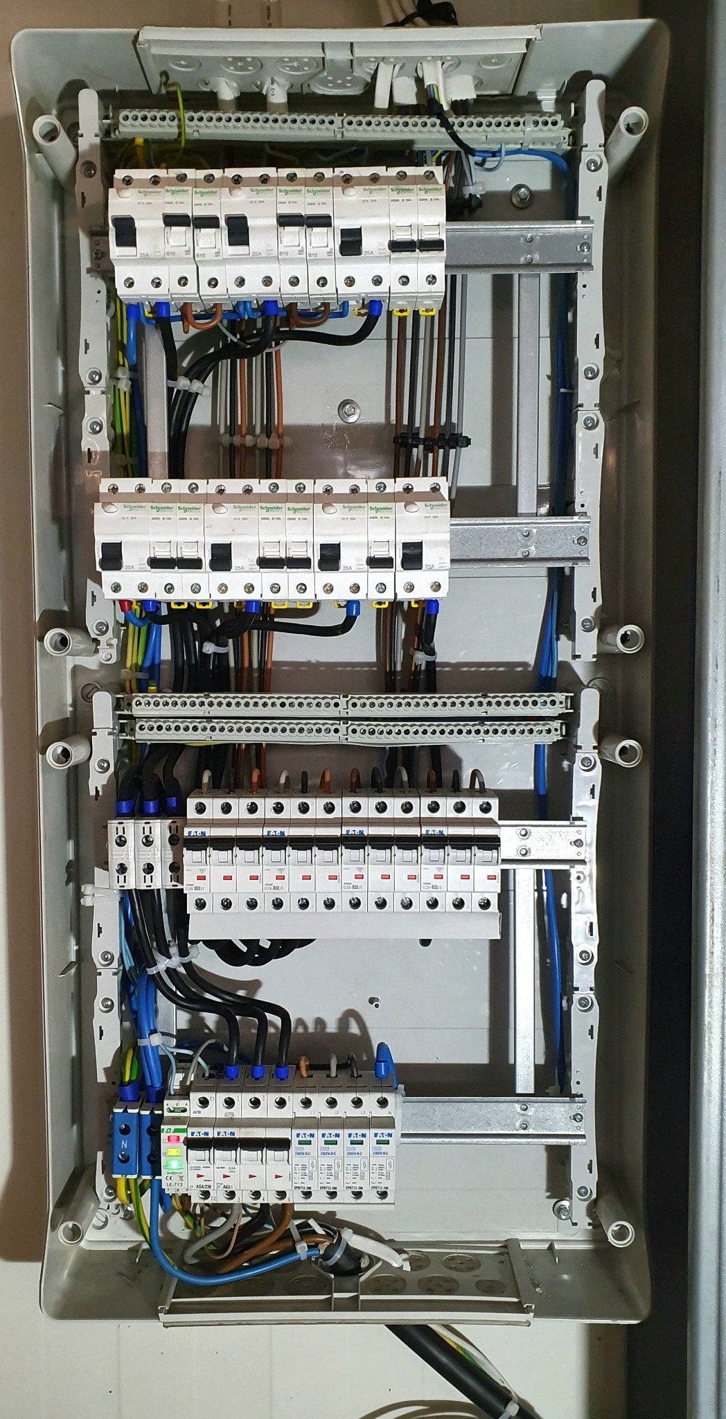 Rozdzielnica elektryczna z zainstalowanymi bezpiecznikami i przewodami, widoczne elementy marki Schneider Electric i Eaton, jeden z bezpieczników z diodą LED świecącą na zielono.