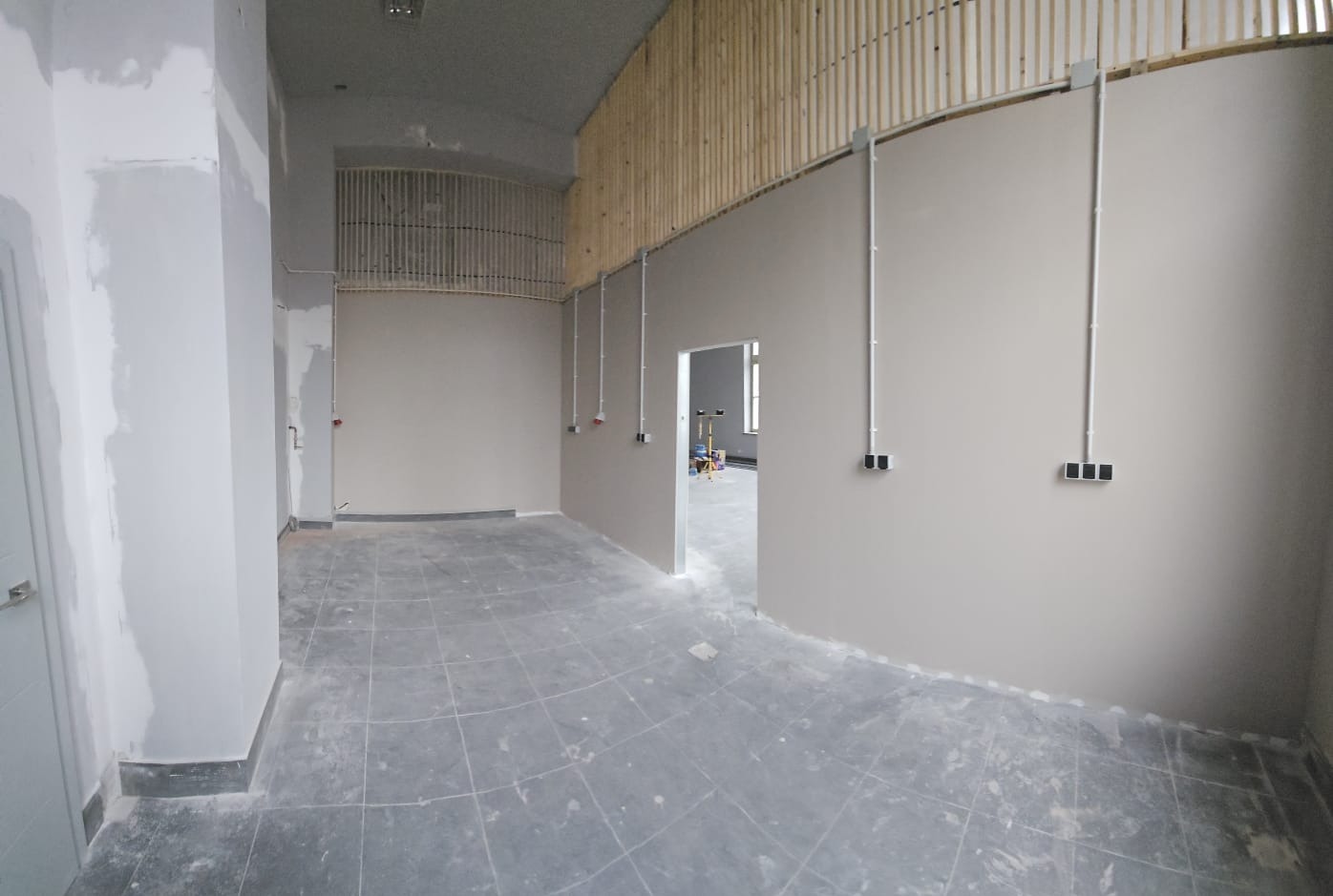 Wnętrze w trakcie remontu: widoczne kable elektryczne prowadzone po ścianach, puszki instalacyjne i drewniane elementy dekoracyjne pod sufitem. Szare płytki na podłodze.