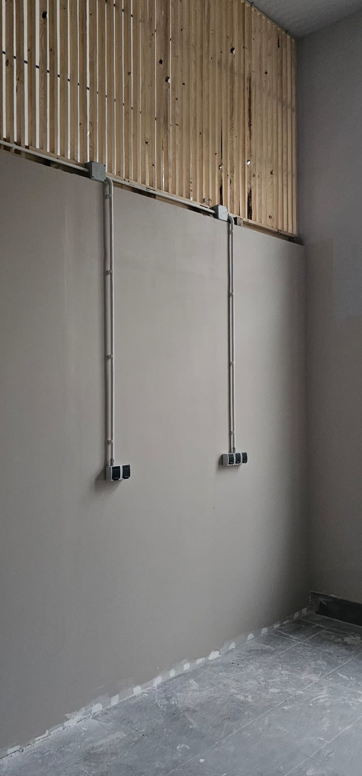 Szare przewody elektryczne w metalowych rurach prowadzone po ścianie w nowym budynku, z widocznymi puszkami i gniazdami. Ściana pomalowana na szaro.