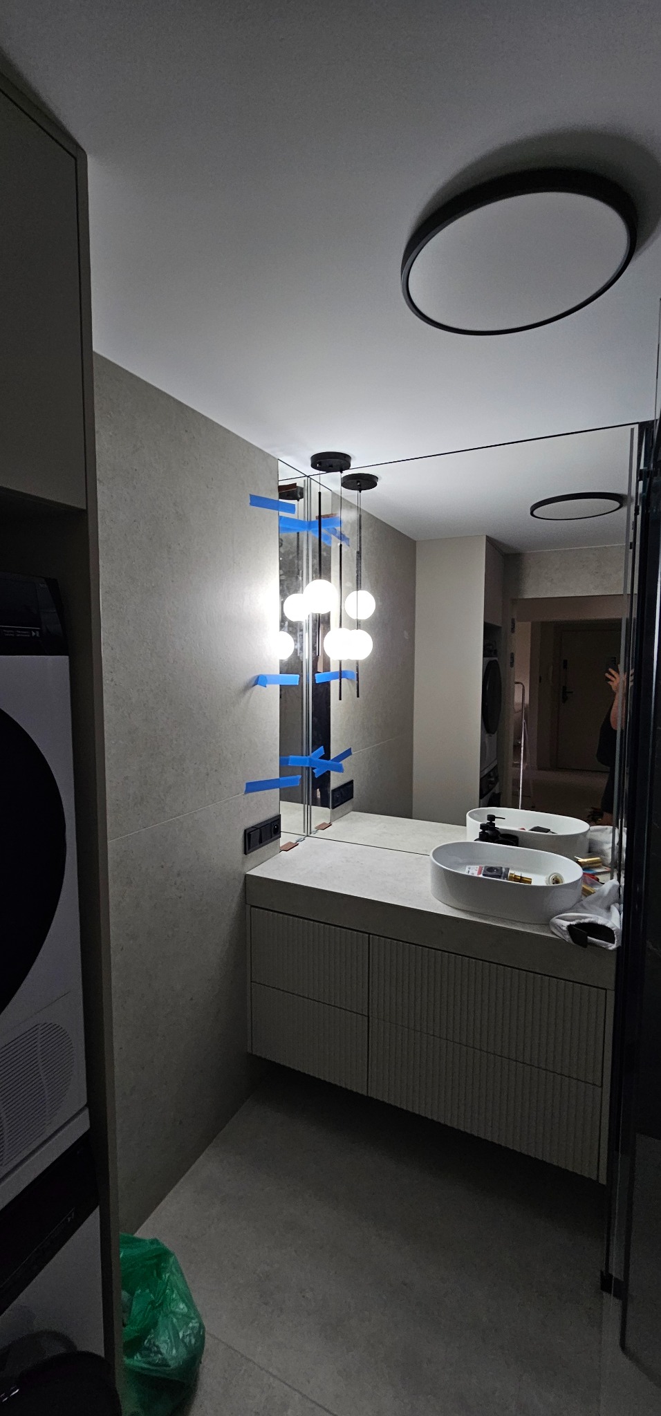 Nowoczesna łazienka w trakcie montażu oświetlenia: lampa wisząca z kulistymi kloszami, mocowana do lustra za pomocą taśmy maskującej.