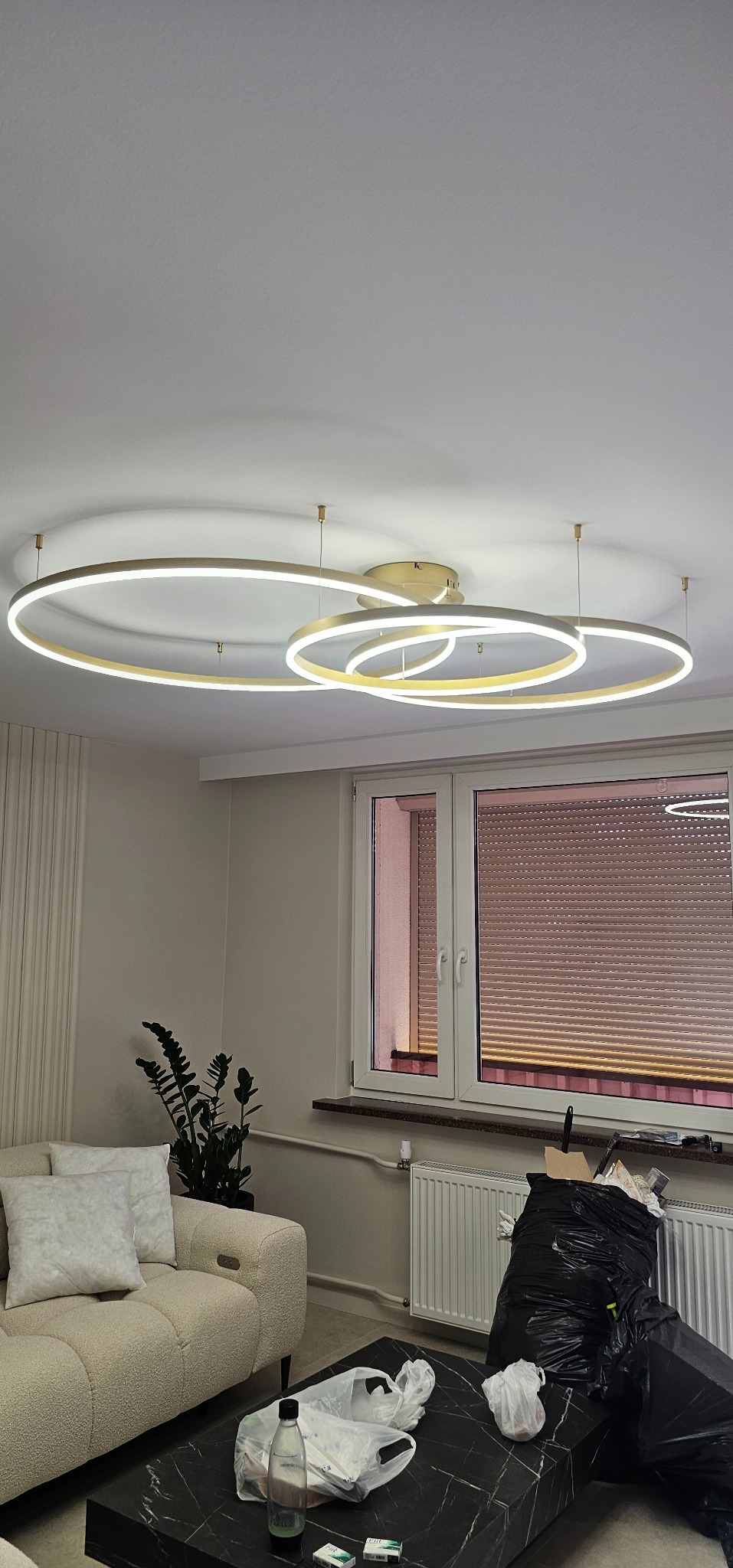 Nowoczesna, złota lampa sufitowa z LED w kształcie obręczy, zamontowana w salonie w Różańsku. Minimalistyczny design oświetlenia.