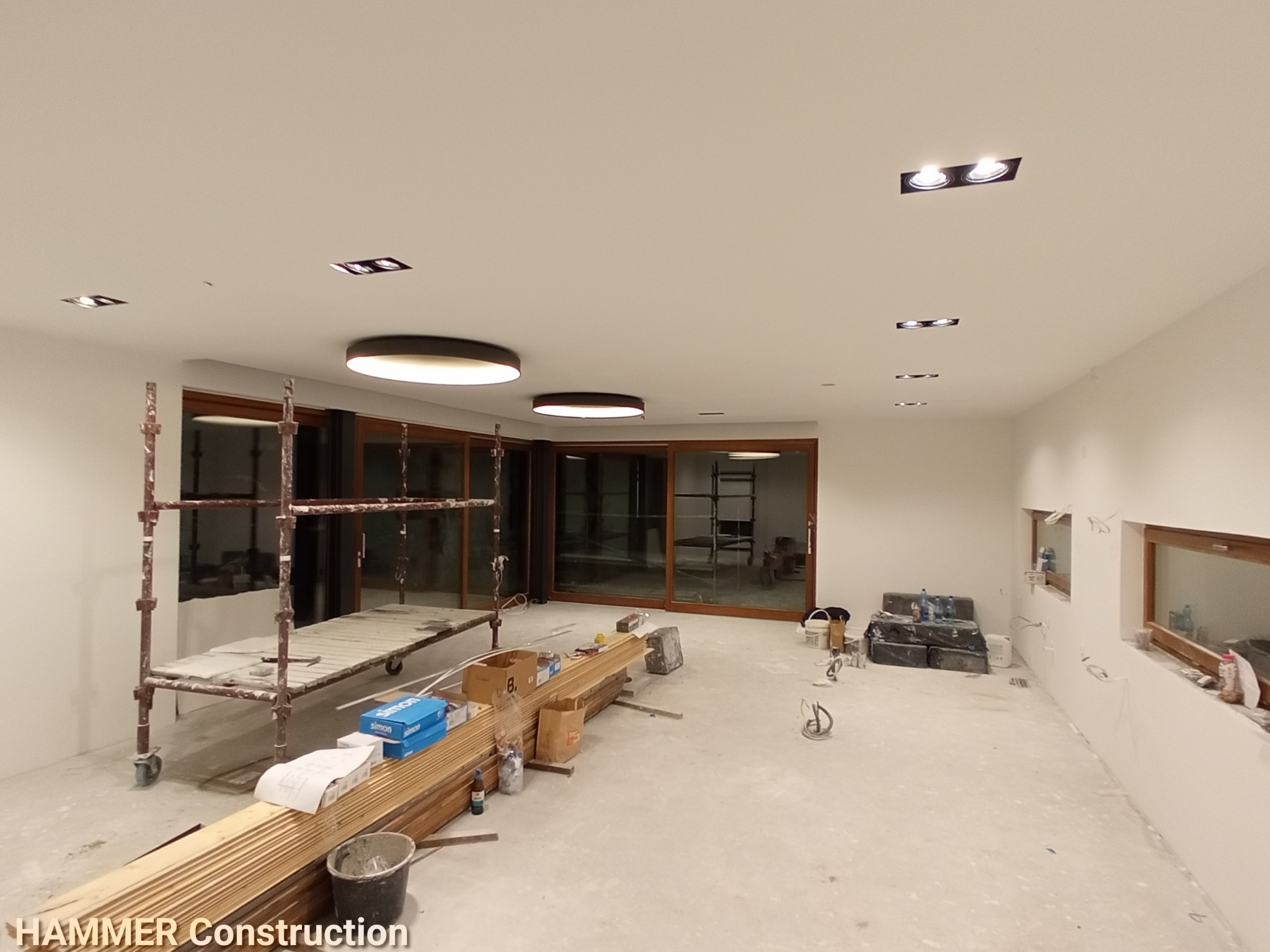 Wnętrze w trakcie prac wykończeniowych: rozstawione rusztowanie, przygotowane deski podłogowe, widoczne puszki elektryczne w ścianie, surowe ściany gotowe do dalszych prac.