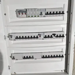 Otwarta skrzynka elektryczna z trzema rzędami bezpieczników i wyłączników różnicowoprądowych marki Legrand, widoczne oznaczenia amperażu i napięcia