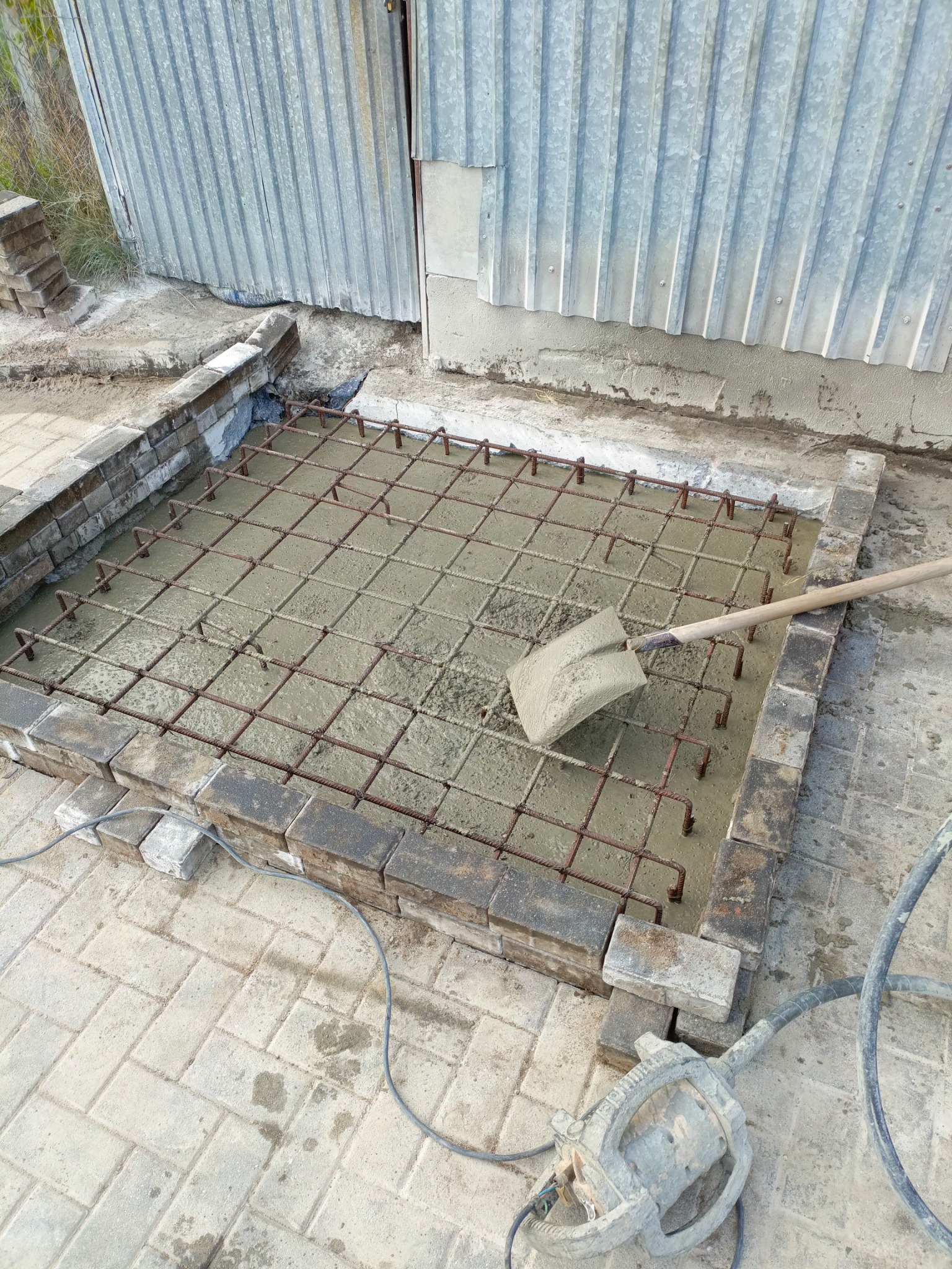 Przygotowanie podłoża pod kostkę brukową: zalewanie betonem zbrojonym siatką stalową, widoczna łopata i zagęszczarka wibracyjna, obrzeże z kostki.