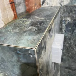 Półka z płytek imitujących marmur w trakcie montażu w łazience, widoczne niedokończone ściany i biała kratka wentylacyjna.