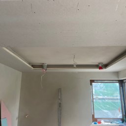 KVB CONSTRUCTION KAMIL VIP BUD Kamil Damps - Sufit podwieszany z płyt gipsowo-kartonowych w trakcie montażu w Gdyni, widoczne kable instalacji elektrycznej, poziomica oparta o ścianę.
