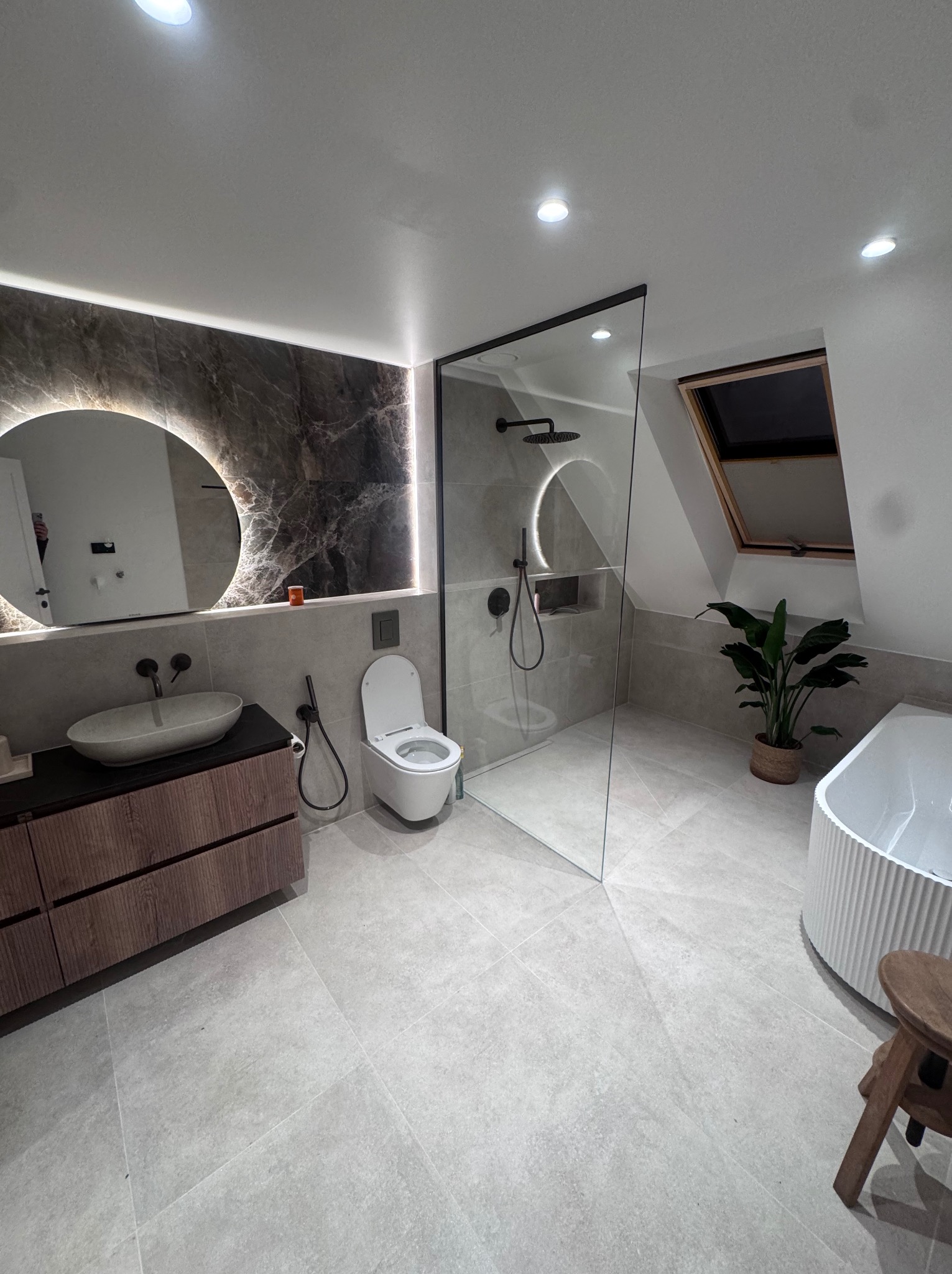 Nowoczesna łazienka na poddaszu z kabiną walk-in, umywalką nablatową, podświetlanym lustrem i oknem dachowym. Minimalistyczny design i stonowana kolorystyka.