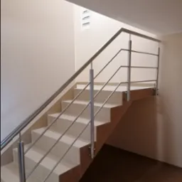 Wewnętrzne schody wyłożone jasnymi płytkami z poręczą ze stali nierdzewnej, widok z dołu na górę.