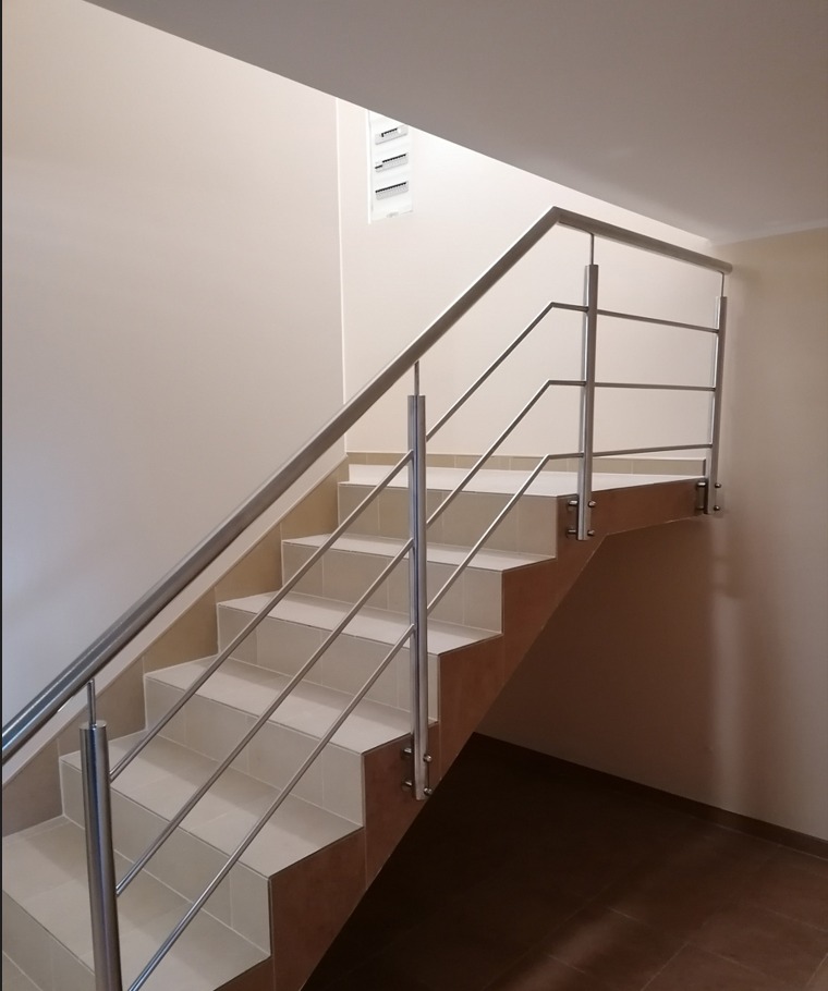 Wewnętrzne schody wyłożone jasnymi płytkami z poręczą ze stali nierdzewnej, widok z dołu na górę.