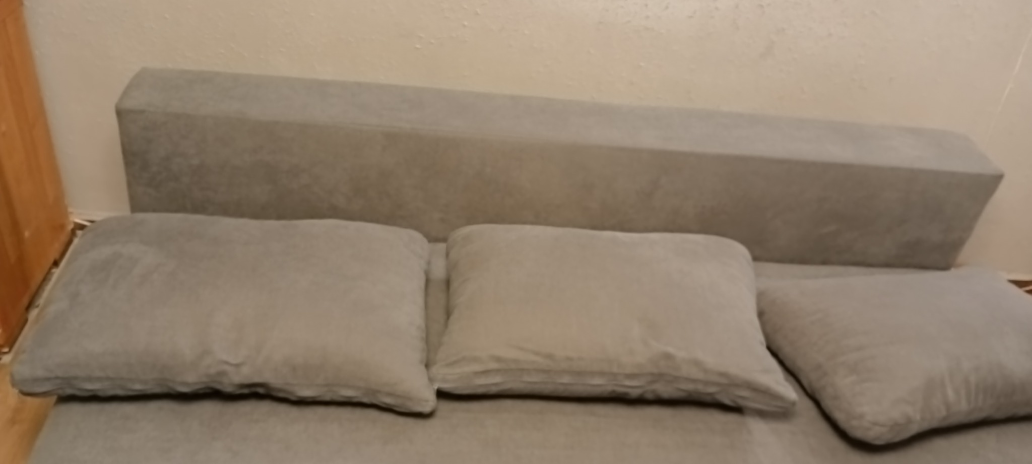 Szara kanapa z trzema poduszkami w pokoju z jasnymi ścianami.