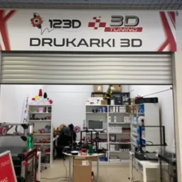 Wnętrze sklepu z drukarkami 3D, widoczne drukarki na stołach i półkach, logo 123D 3D Tuning nad wejściem, punkt nadawania paczek DPD.