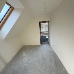 SZYMBUD USŁUGI OGÓLNOBUDOWLANE SZYMON SZYMICHOWSKI - Poddasze po remoncie: gładkie, pomalowane ściany w jasnym odcieniu, surowa betonowa podłoga, okno dachowe i balkonowe z widokiem na drzewa.