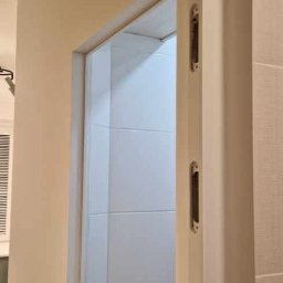 SZYMBUD USŁUGI OGÓLNOBUDOWLANE SZYMON SZYMICHOWSKI - Zamontowane drzwi przesuwne w łazience z wykończeniem w beżowych i białych płytkach.