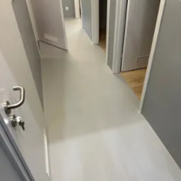 Korytarz po remoncie z szarą podłogą z żywicy epoksydowej, widoczne drzwi z metalowymi klamkami i kluczami w zamku, w tle fragment podłogi wyłożonej panelami.