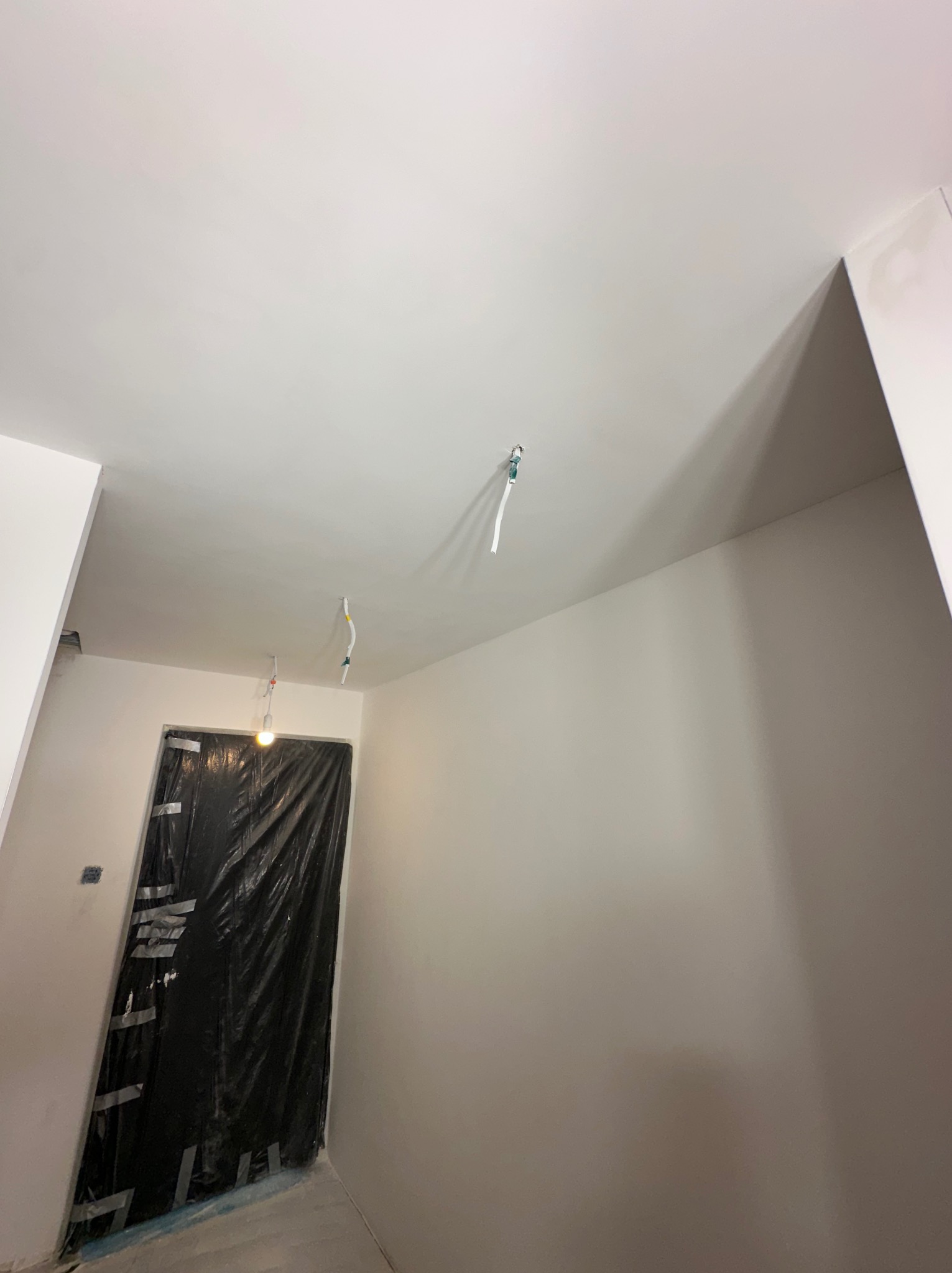 Wnętrze w trakcie remontu: świeżo pomalowane ściany i sufit na biało, zabezpieczone folią drzwi, widoczne wystające kable oświetleniowe.