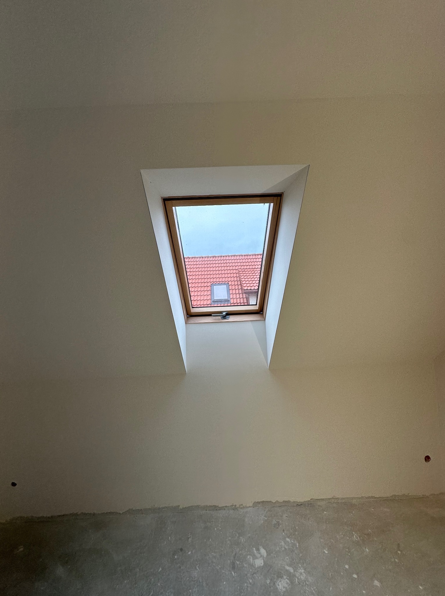 Ściana poddasza z oknem dachowym przed malowaniem: widoczna struktura gładzi, surowy beton u dołu ściany i wystający kabel.