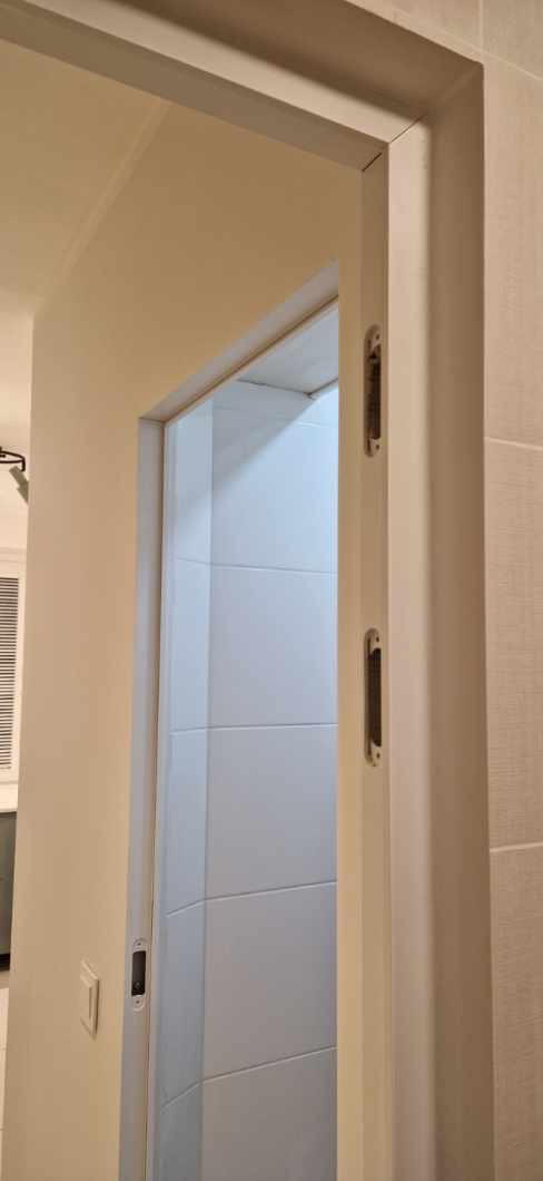 Zamontowane drzwi przesuwne w łazience z wykończeniem w beżowych i białych płytkach.