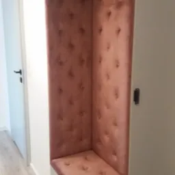 Wnęka z siedziskiem obita różowym welurem z guzikami, wbudowana w szafę w przedpokoju, widoczne drzwi i fragment podłogi.