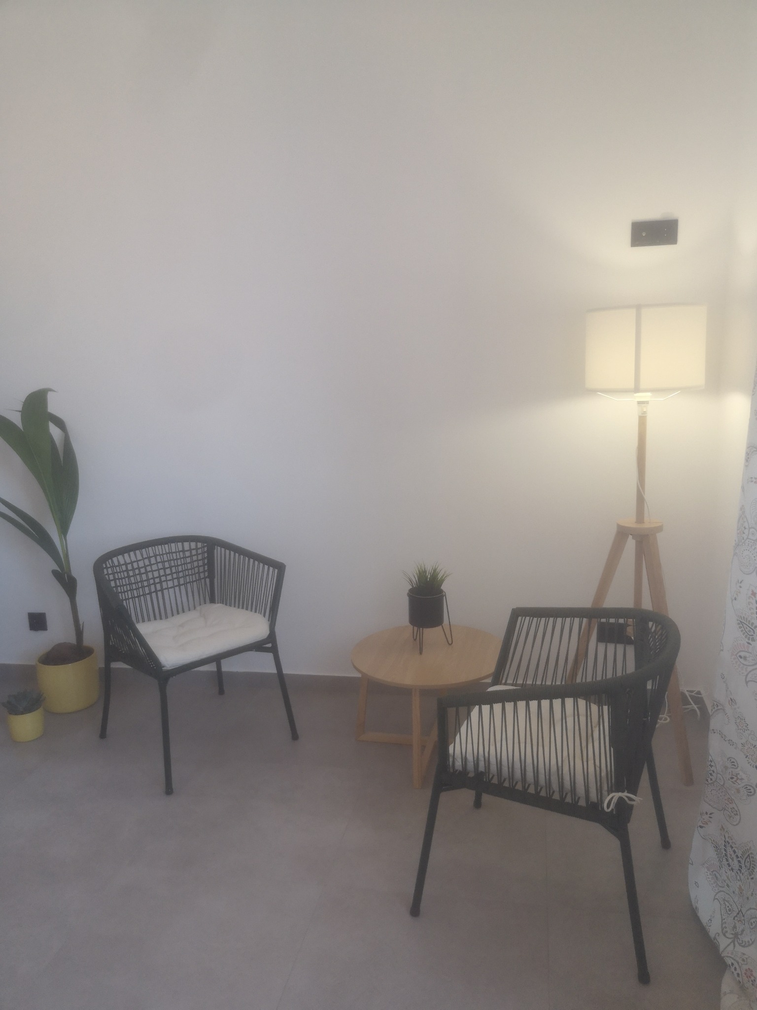 Ustawienie poczekalni z dwoma plecionymi krzesłami z poduszkami, małym okrągłym stolikiem z rośliną w doniczce i wysoką lampą podłogową w gabinecie w Krotoszynie.