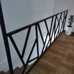 Nowoczesna, czarna balustrada schodowa z geometrycznym wzorem w Złoczewie, widok z g&oacute;ry na drewnopodobne płytki podłogowe i schody.