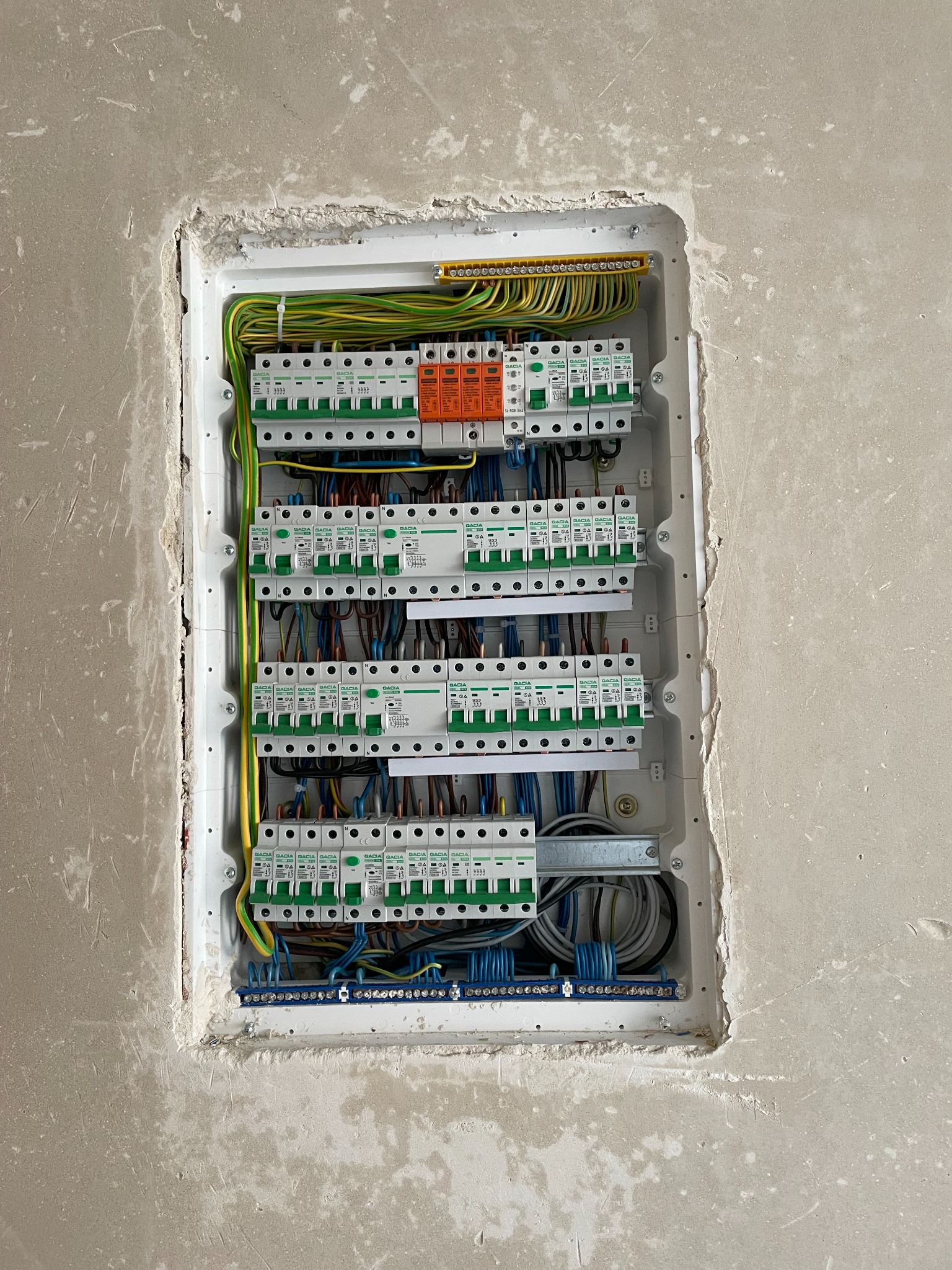 Rozdzielnica elektryczna Gacia z zabezpieczeniami, zamontowana w surowej ścianie. Widoczne przewody, bezpieczniki i listwy zaciskowe. Instalacja w trakcie prac wykończeniowych.