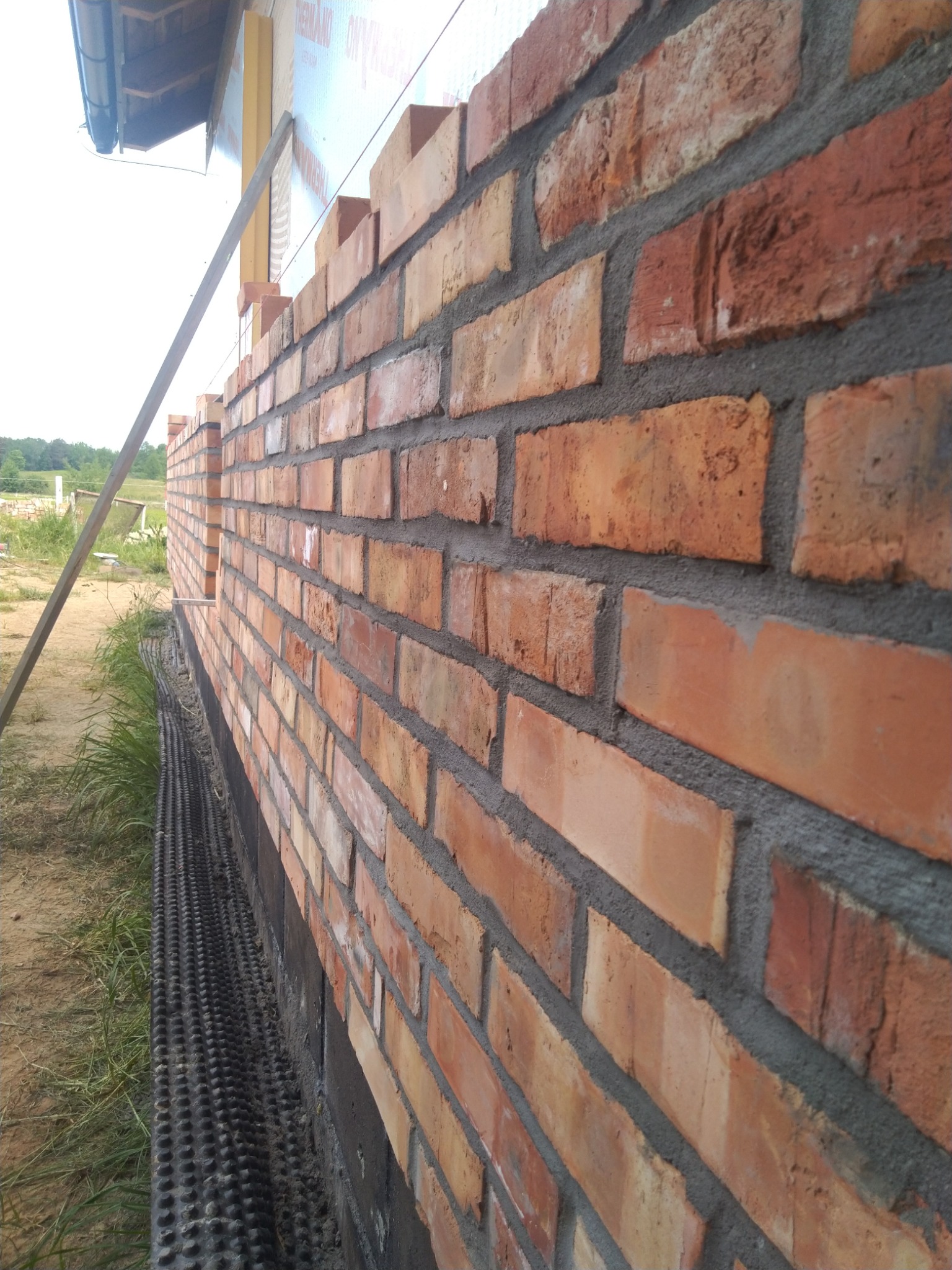 Świeżo wymurowana ściana z czerwonej cegły z widoczną izolacją fundamentu i poziomowaniem na budowie.