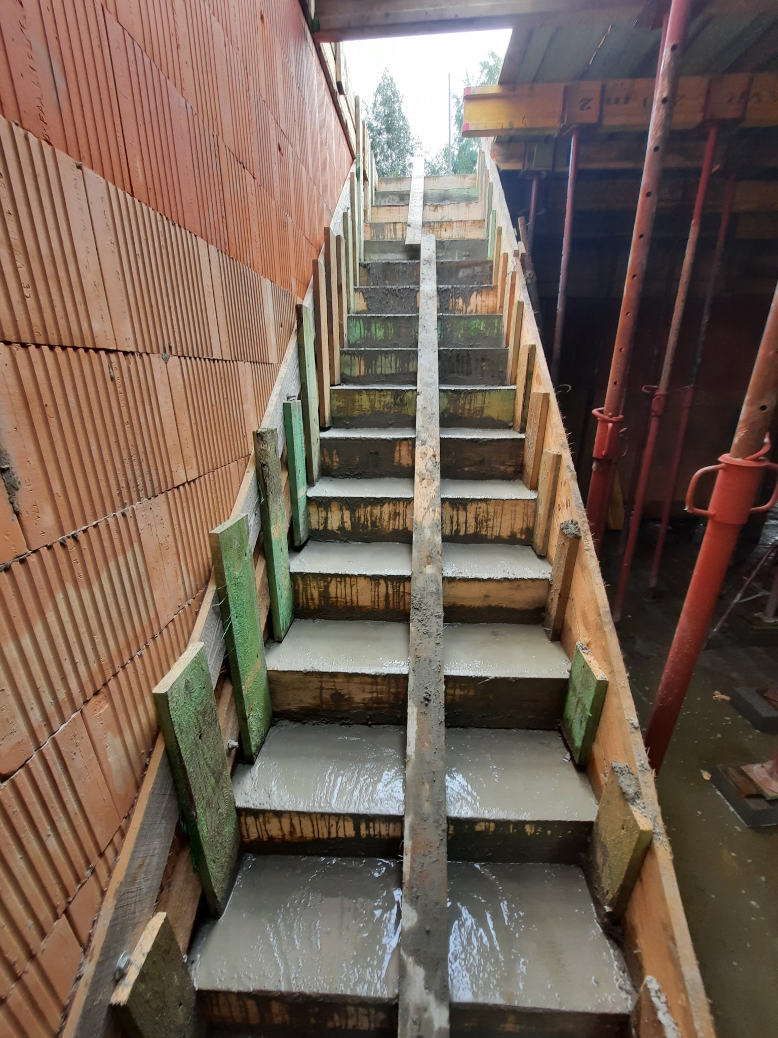 Budowa betonowych schodów wewnątrz powstającego domu z cegły w Żabiej Woli, widoczne szalunki i podpory.