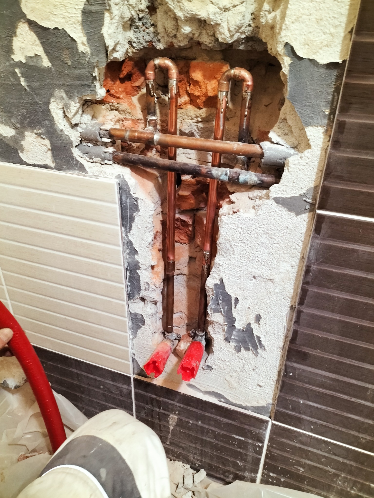 Odsłonięte miedziane rury instalacji wodnej w ścianie podczas remontu w Białogardzie, widoczne uszkodzenia tynku i fragmenty płytek.
