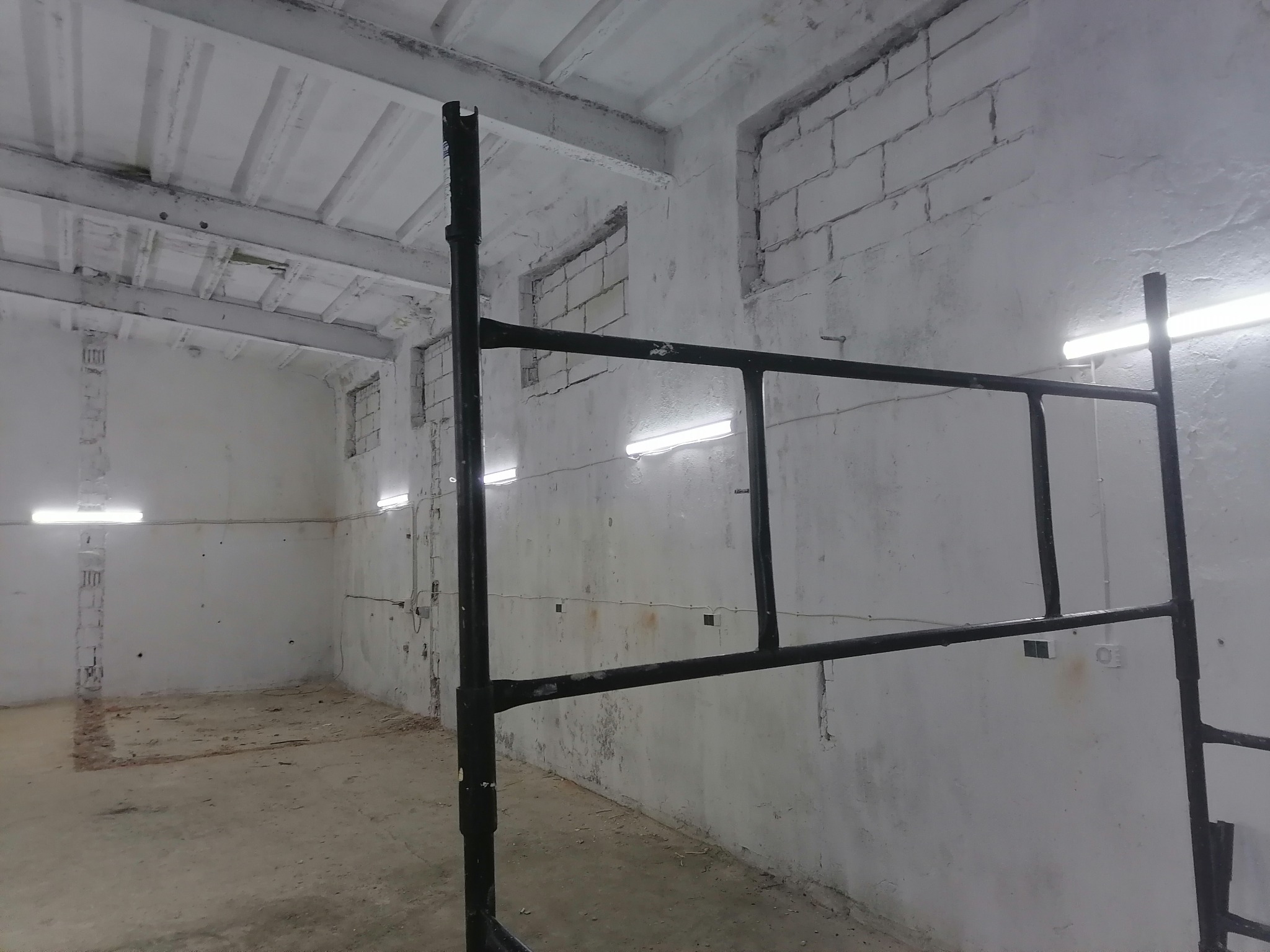 Wnętrze w trakcie remontu, widoczne rusztowanie na pierwszym planie, surowe ściany z cegły i widoczne instalacje elektryczne
