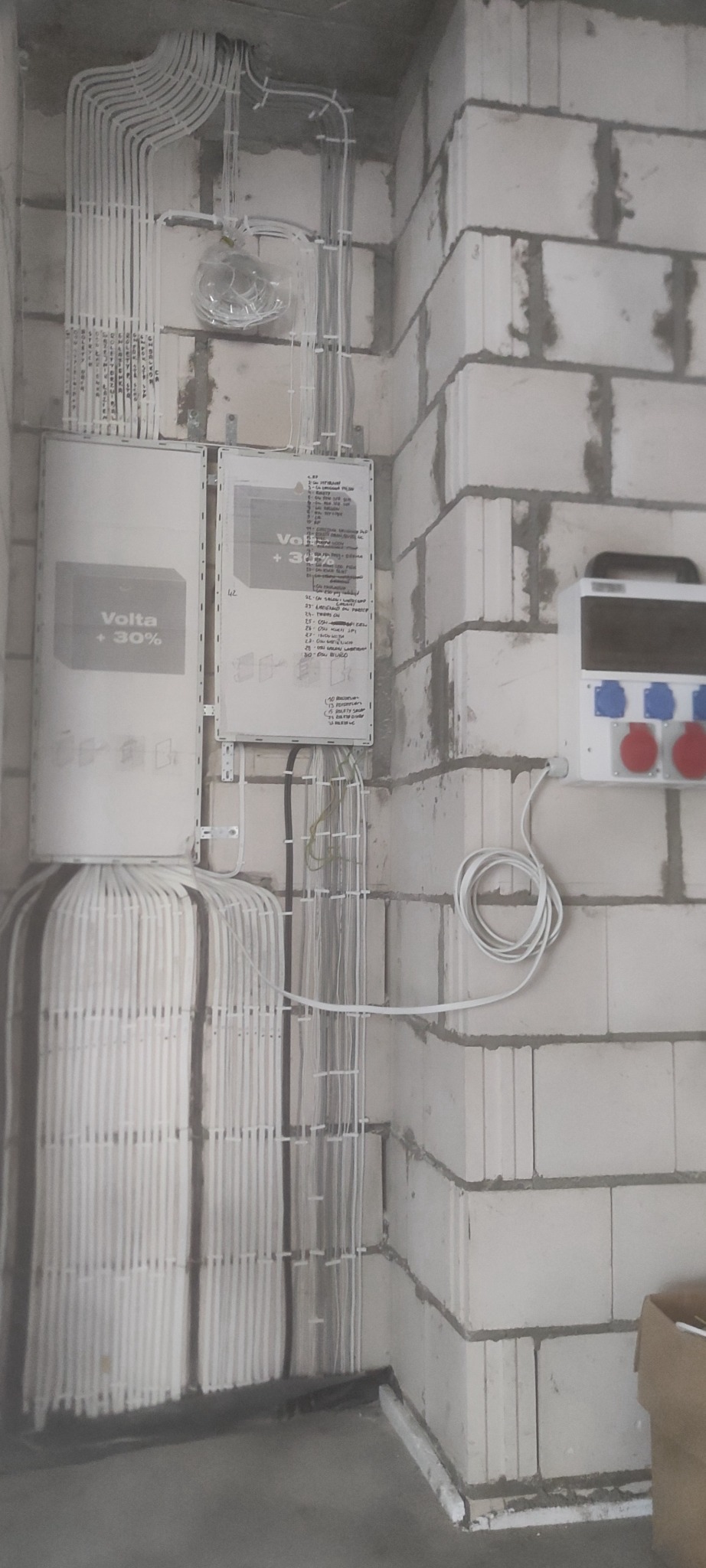Rozdzielnice elektryczne Volta +30% zamontowane na ścianie z betonu komórkowego, widoczne liczne białe przewody ułożone w peszlach i korytkach, dodatkowe gniazdo siłowe na ścianie.