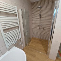 Haustechnik REMONTY I WYKOŃCZENIA Andrzej Dychus - Nowoczesna łazienka z kabiną prysznicową typu walk-in, grzejnikiem drabinkowym i wanną, wykończona płytkami w odcieniach beżu i brązu z drewnopodobną podłogą i odpływem liniowym