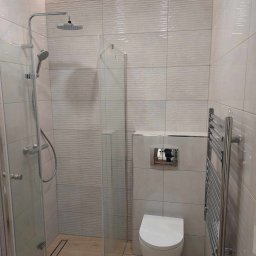 Haustechnik REMONTY I WYKOŃCZENIA Andrzej Dychus - Nowoczesna łazienka z kabiną prysznicową typu walk-in, podwieszaną miską WC, grzejnikiem drabinkowym i płytkami z subtelnym falistym wzorem oraz oświetleniem LED podsufitowym.