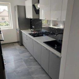 Haustechnik REMONTY I WYKOŃCZENIA Andrzej Dychus - Nowoczesna kuchnia z szarymi szafkami, białymi górnymi szafkami, czarnym blatem imitującym marmur i szarą podłogą z płytek imitujących kamień.