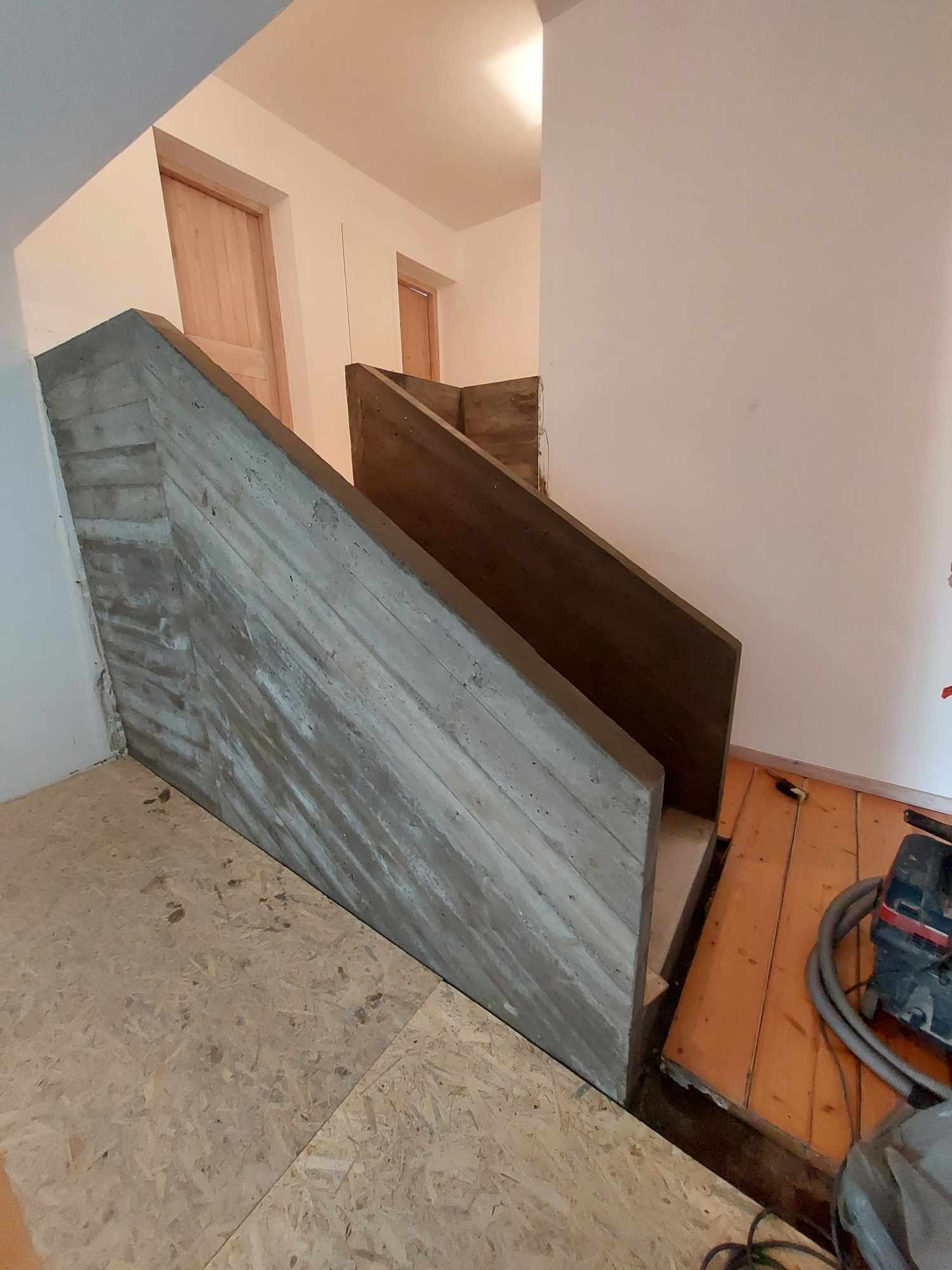 Surowe betonowe schody z drewnianymi elementami w trakcie budowy, widoczne narzędzia i niezabezpieczona podłoga.