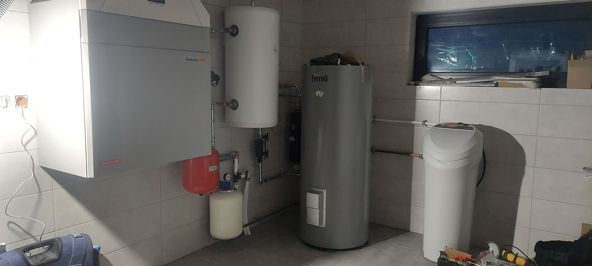 Kotłownia z piecem gazowym, zasobnikami ciepłej wody i stacją uzdatniania wody, instalacja w pomieszczeniu wyłożonym płytkami ceramicznymi.