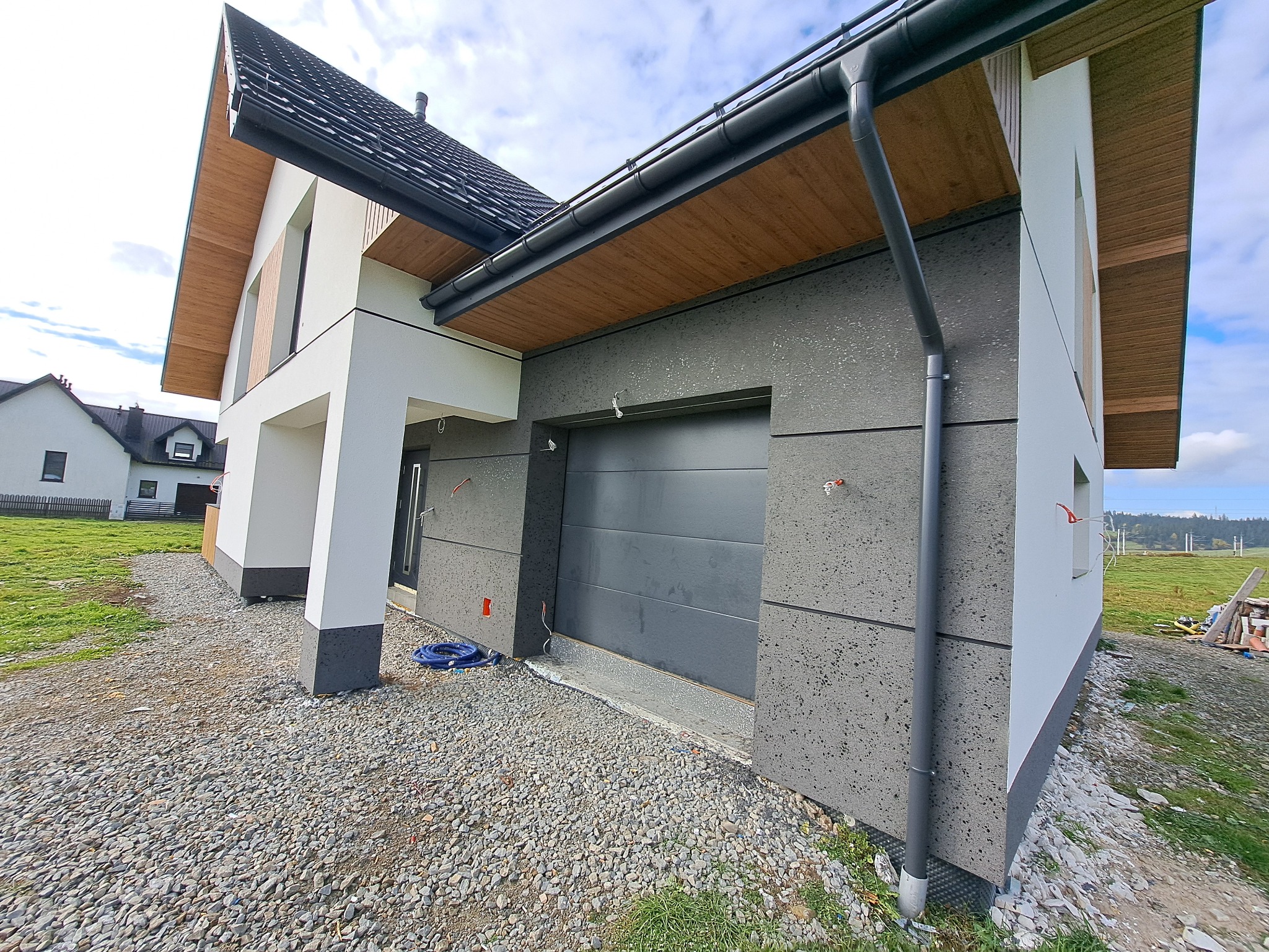 Nowoczesny dom jednorodzinny z garażem w Raba Wyżna. Elewacja w odcieniach szarości i bieli, widoczne detale wykończeniowe, dachówka w kolorze grafitowym.