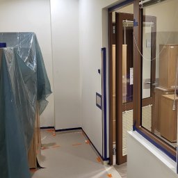 Karl BUD Karol Pniewski - Przygotowanie do malowania w biurze: ściany i framugi oklejone taśmą malarską, meble zabezpieczone folią ochronną.