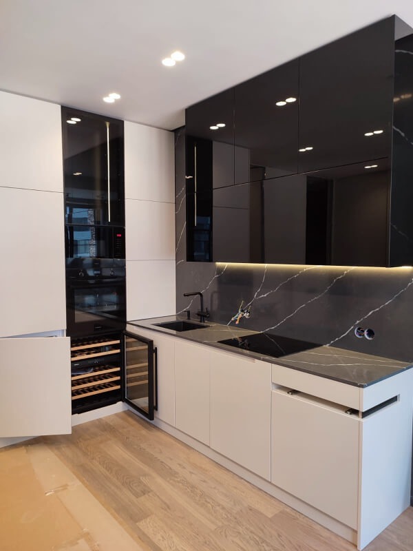 Nowoczesna kuchnia z białymi i czarnymi szafkami, blatem z efektem marmuru, otwartą szafką na wino i drewnianą podłogą.