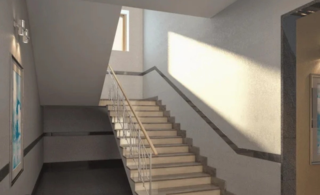 Klatka schodowa w budynku mieszkalnym z jasnymi schodami, metalową balustradą i dekoracyjną listwą na ścianie, oświetlona naturalnym światłem z okna.