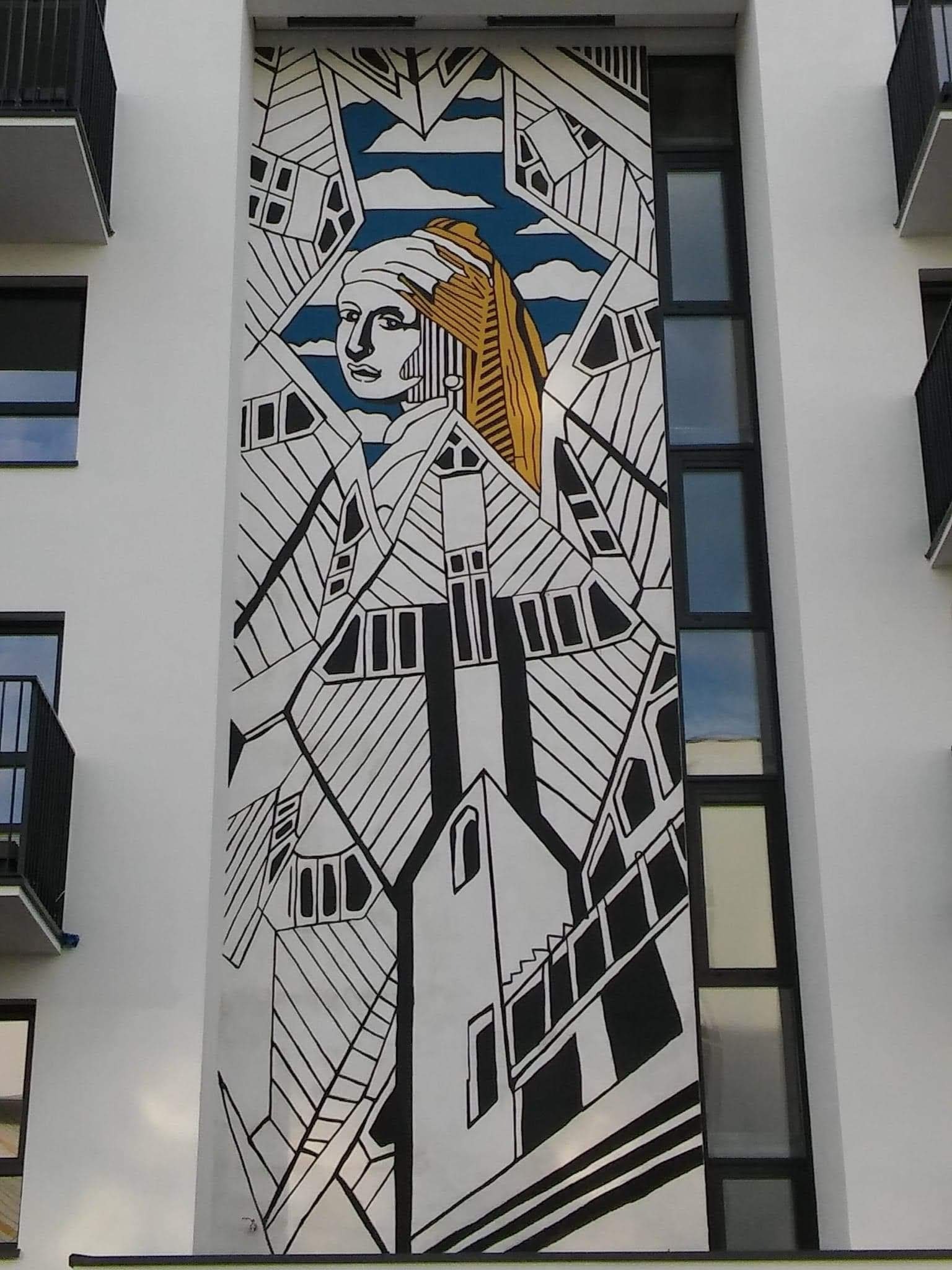 Mural na ścianie budynku przedstawiający stylizowaną wersję obrazu 'Dziewczyna z perłą' Vermeera, wkomponowaną w geometryczne wzory przypominające architekturę miejską.