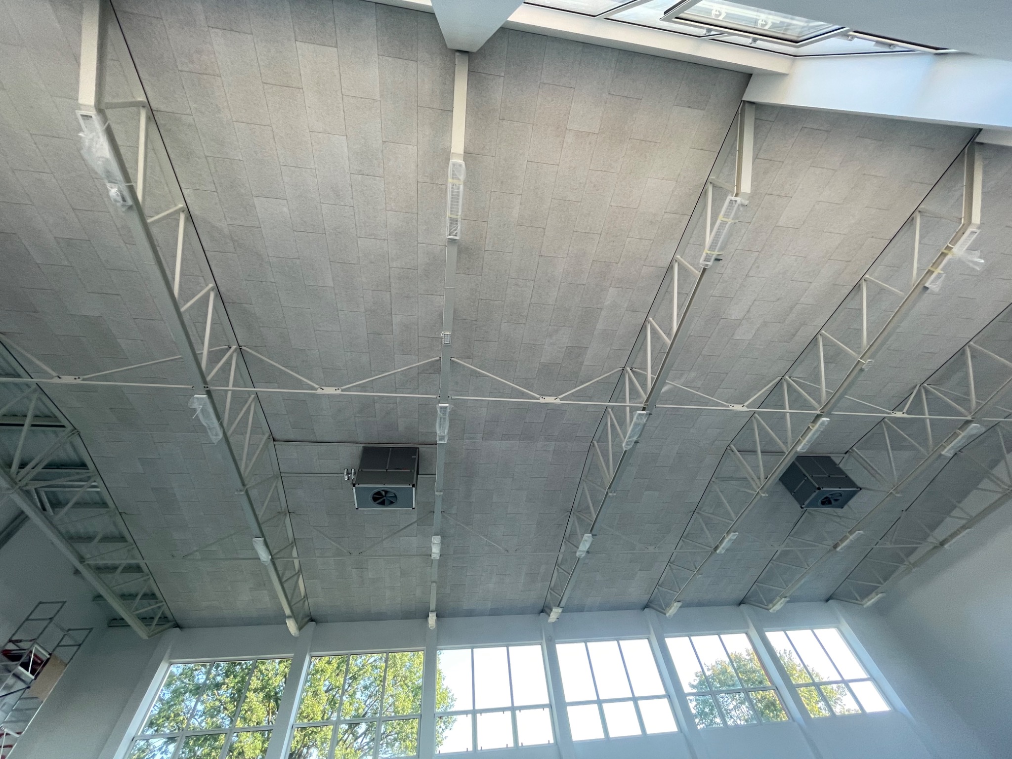 Sufit z płyt akustycznych w dużej hali, widok z dołu, widoczne elementy konstrukcyjne i system wentylacji.