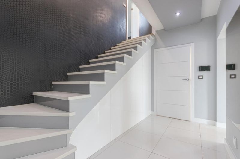 Nowoczesne schody w jasnych szarościach i bieli, z ciemnoszarą ścianą o wzorze plastra miodu, prowadzące na górę, z białą podłogą i drzwiami po prawej stronie.