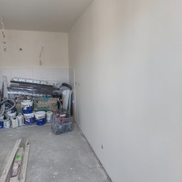 Spontanbud - Świeżo pomalowane ściany w pomieszczeniu w trakcie remontu, widoczne narzędzia malarskie, puszki z farbą i szpachla. Przygotowania do dalszych prac wykończeniowych.