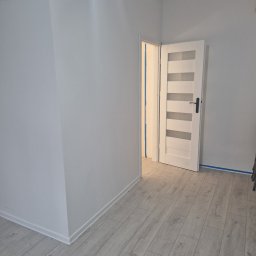 Spontanbud - Jasne wnętrze po remoncie: białe ściany, panele podłogowe. Nowe, białe drzwi z przeszkleniami. Taśma malarska zabezpiecza krawędzie. Minimalistyczny styl.