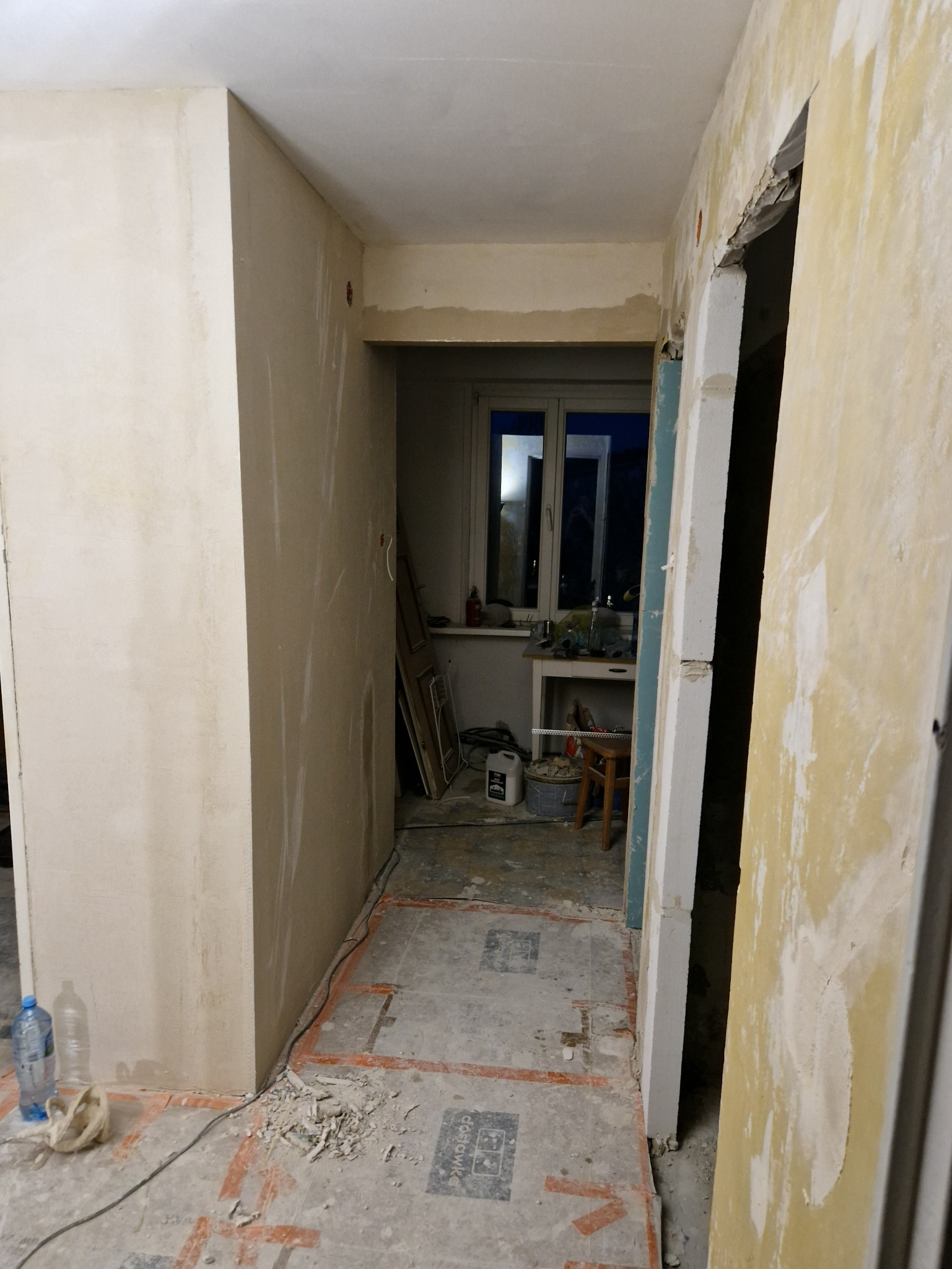 Wnętrze w trakcie prac wykończeniowych: ściany po szpachlowaniu, przygotowane do malowania, widoczne ślady po instalacji ogrzewania podłogowego, okno w tle.