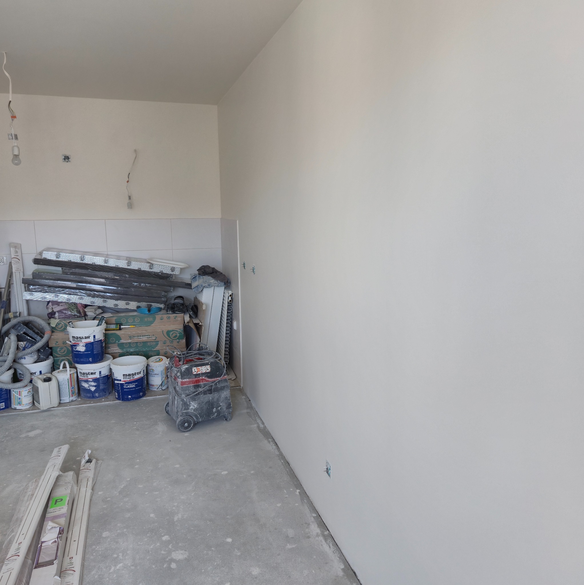 Świeżo pomalowane ściany w pomieszczeniu w trakcie remontu, widoczne narzędzia malarskie, puszki z farbą i szpachla. Przygotowania do dalszych prac wykończeniowych.